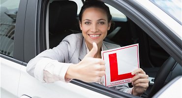 Young female student holding L plate and giving thumbs up 
